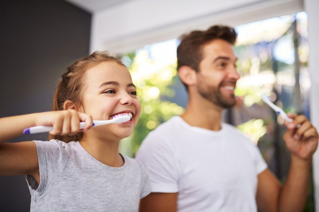Cropped shot of a handsome Dad and his daughter brushing their teeth in the bathroom general dentistry dentist in Towson Maryland